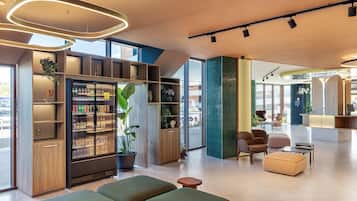 A modern hotel lobby with seating, a reception desk, and a refrigerator stocked with beverages.