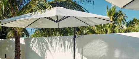 A poolside area with lounge chairs, umbrellas, and potted plants.