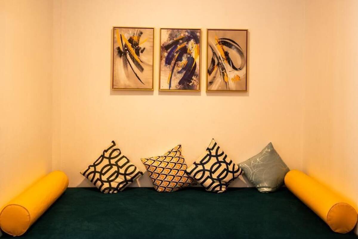 Ein Zimmer mit einem grünen Sofa, gemusterten Kissen, abstrakter Wandkunst und einem Deckenventilator.