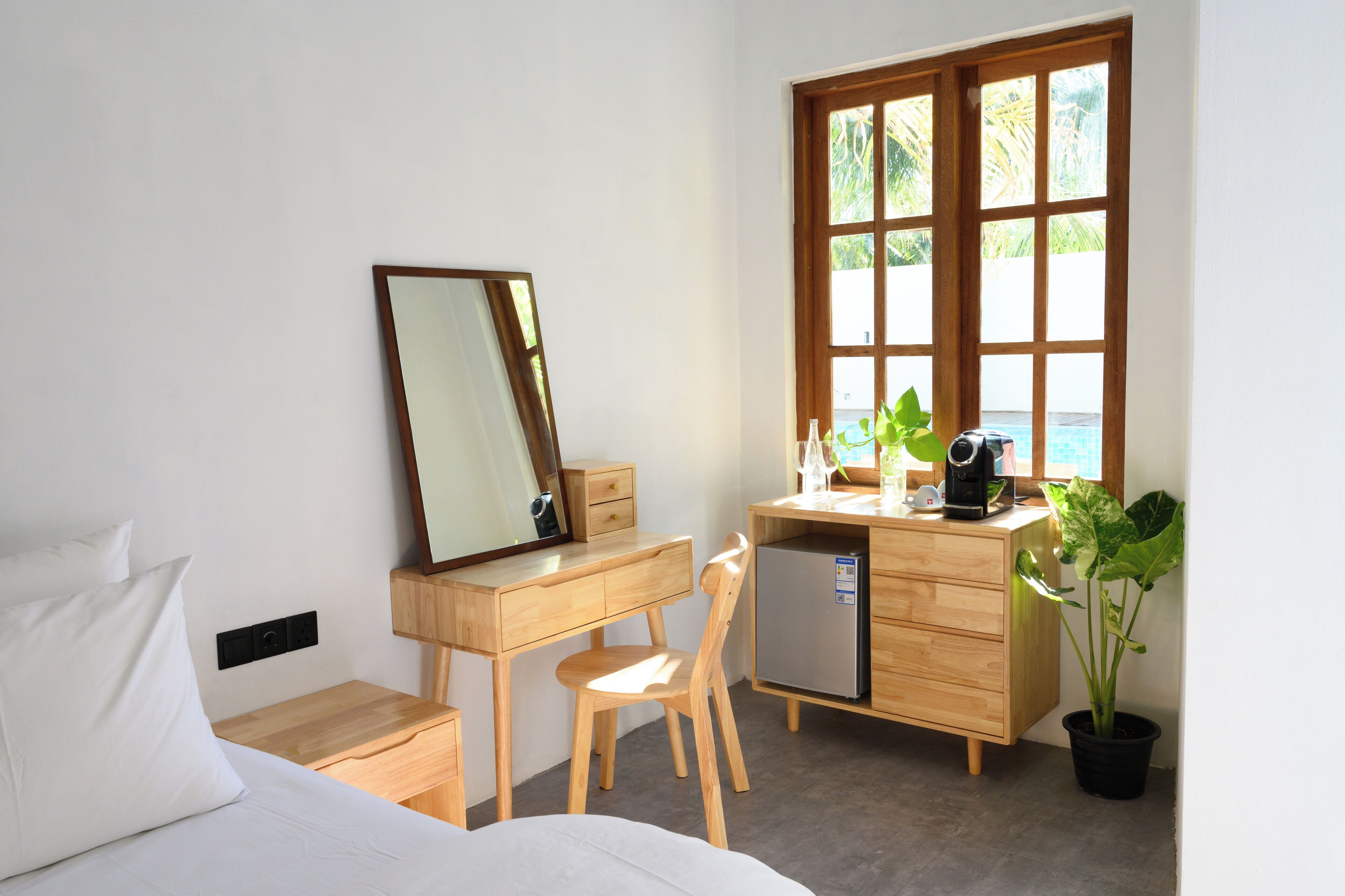 Een kleine hotelkamer met een bed, een bureau met spiegel, een kleine koelkast en een potplant.