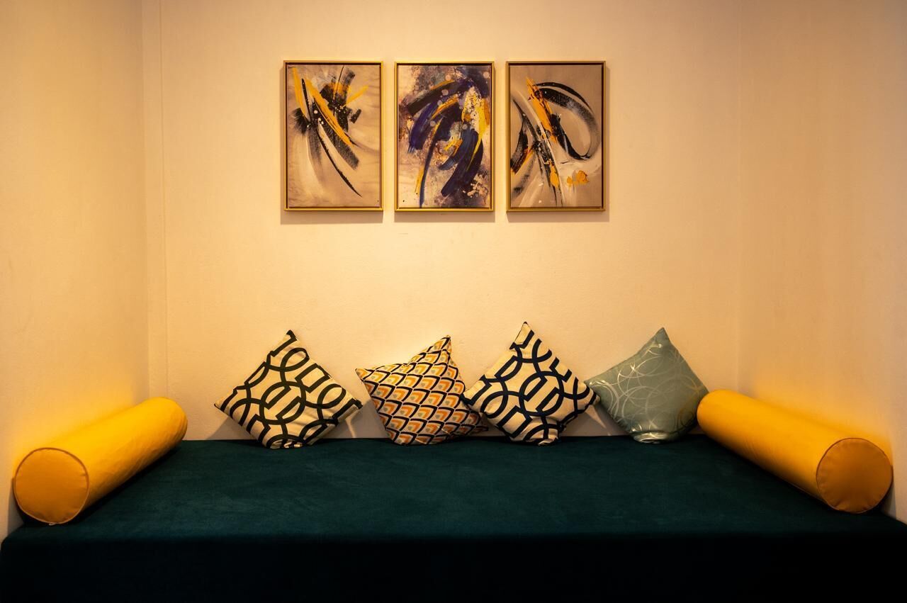 A room with a green sofa, four patterned pillows, and three abstract paintings on the wall.