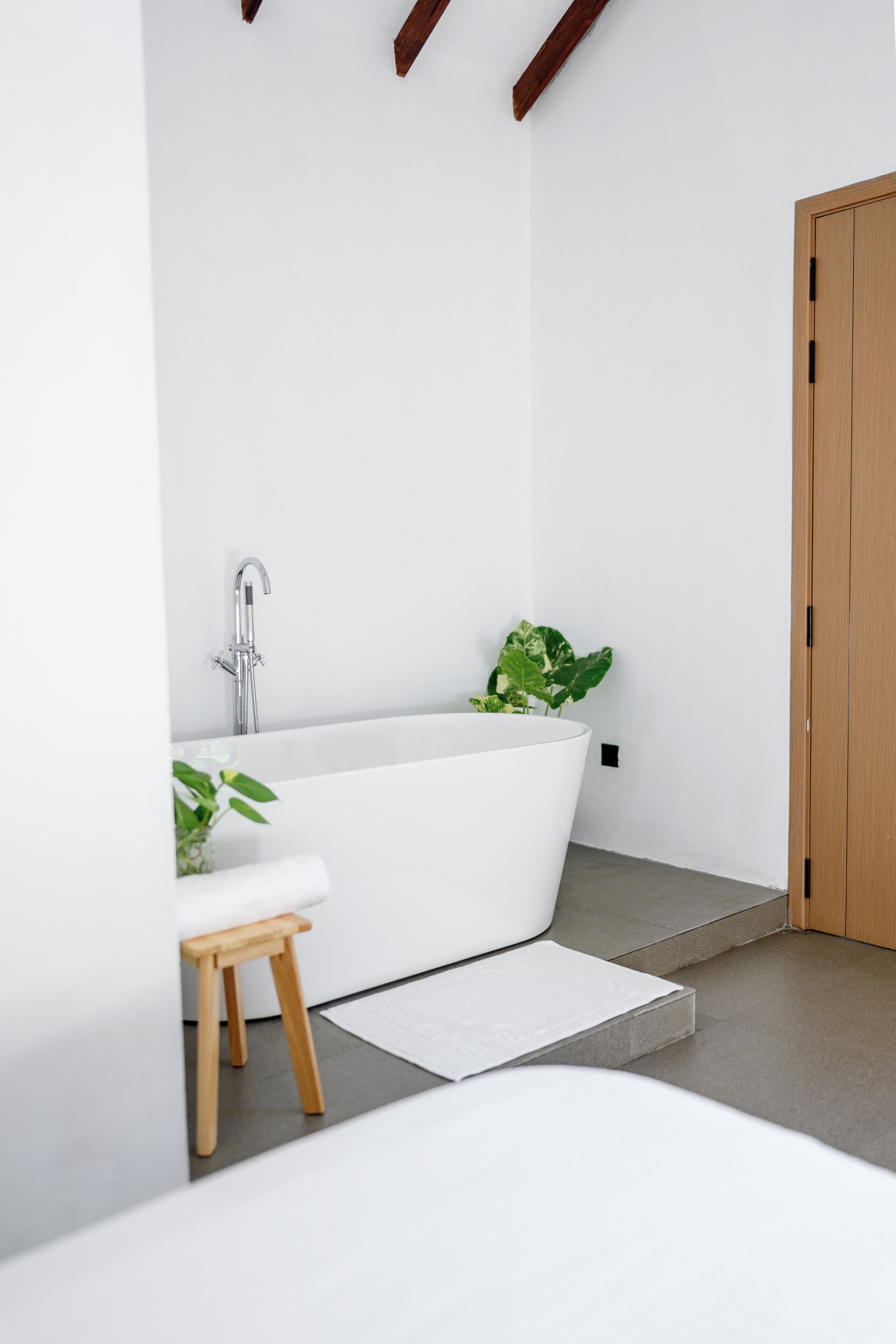 Een moderne badkamer met een vrijstaand bad, een houten krukje en een potplant.