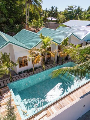 A swimming pool with a tiled deck, surrounded by palm trees and a building with a green roof. - Kondey Villas (Kondey)