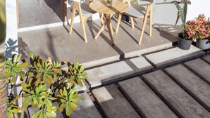 A small patio with a wooden table and chairs, surrounded by potted plants and a window with wooden bars. - Kondey Villas (Kondey)