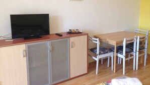 A small room with a wooden cabinet, a television, a small table with chairs, and a framed picture on the wall. - Beautiful Apartment With View (Porec)