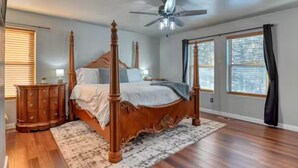 Ein Schlafzimmer mit einem Himmelbett, Deckenventilator, einem Holzschrank und großen Fenstern.