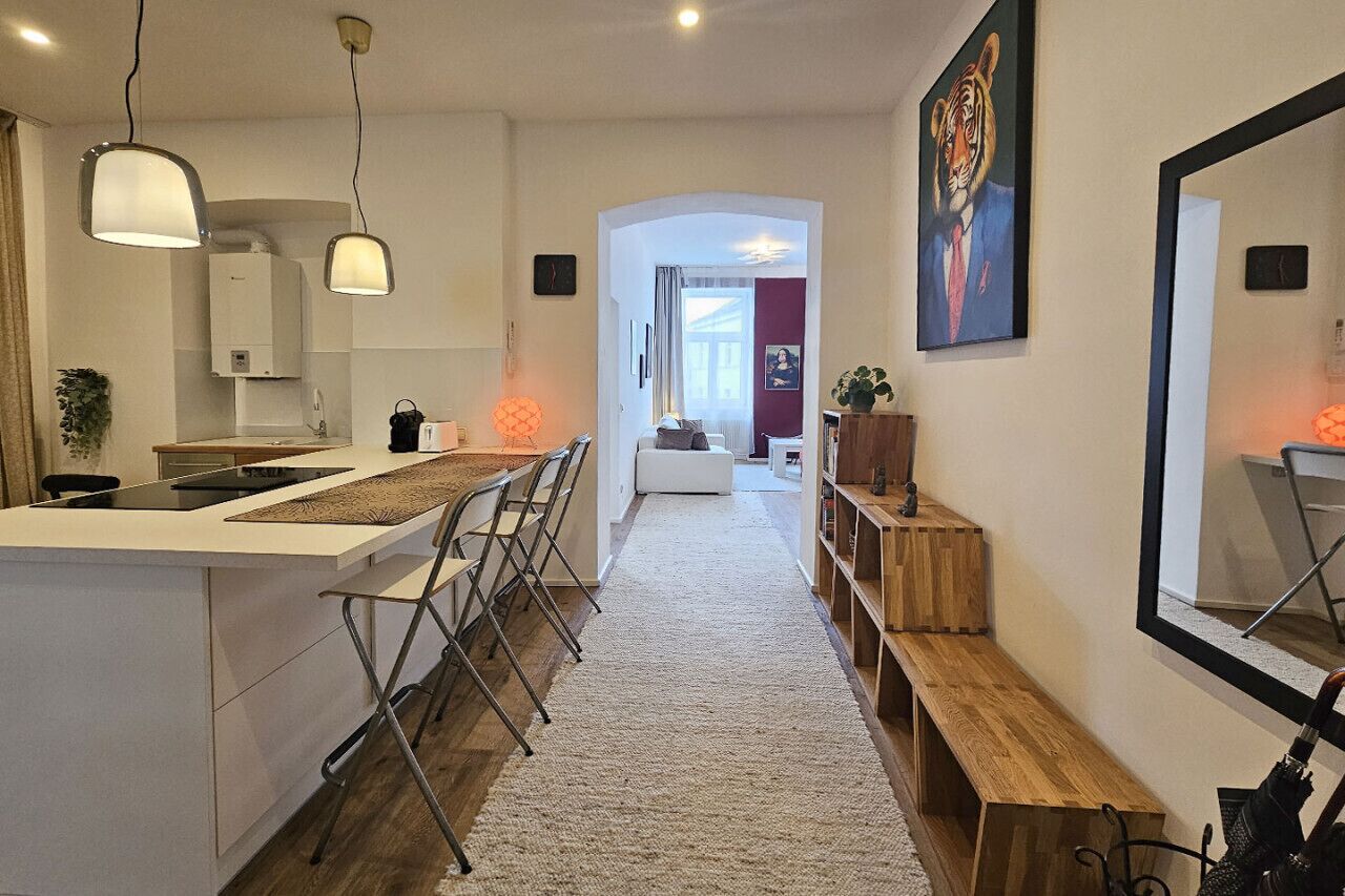 Una cocina moderna con una isla central, luces colgantes y un pasillo que conduce a un dormitorio.