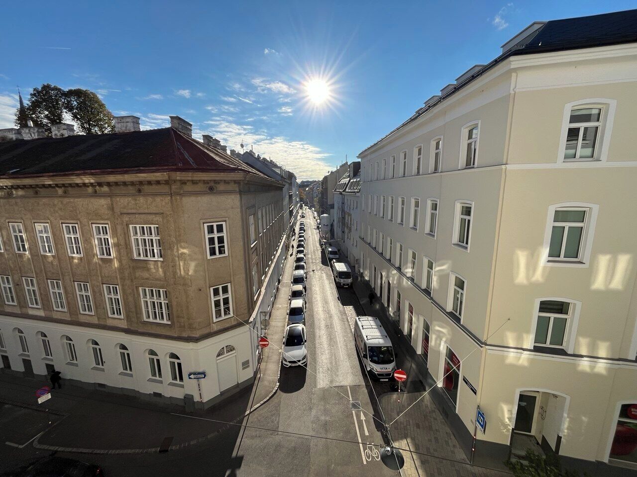 Katunäkymä, jossa näkyy rakennuksia, parkkeerattuja autoja ja kirkas taivas.