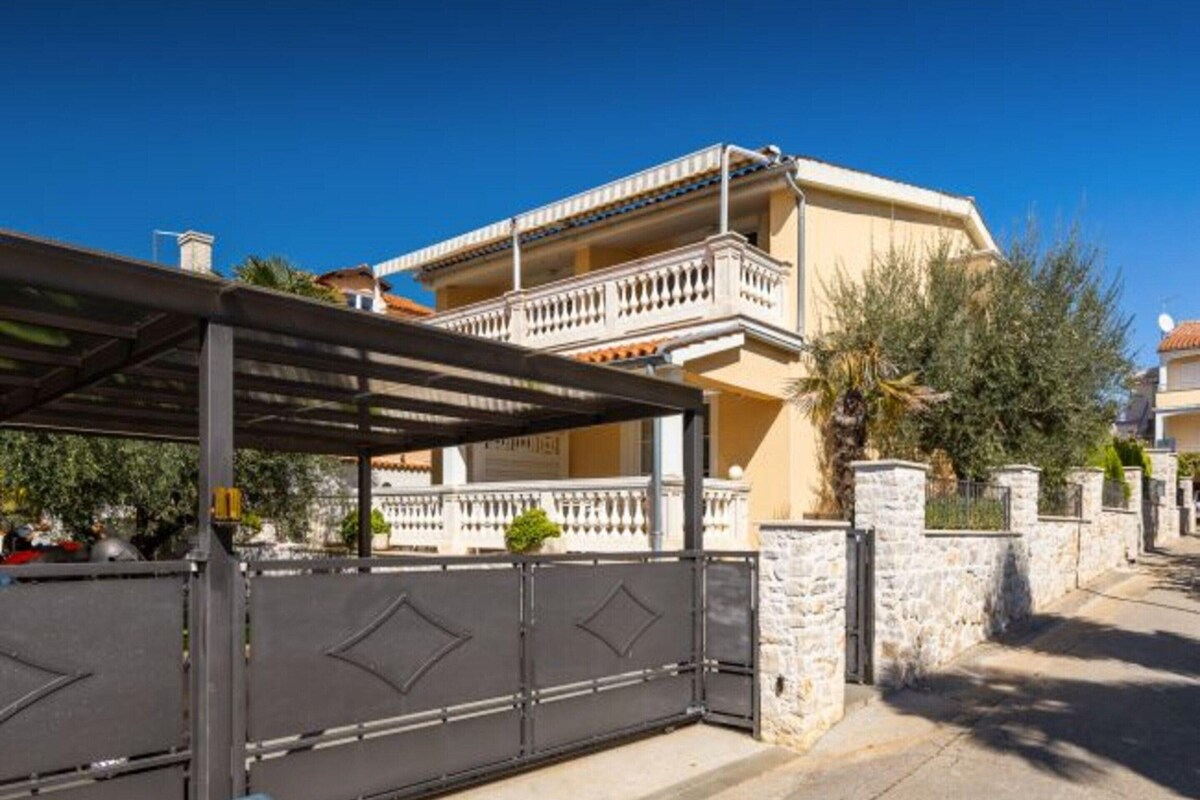 A two-story building with a balcony, stone walls, and a gated entrance.