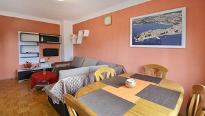 Ein gemütlicher Wohnraum mit Esstisch, Stühlen, einer Couch, einem Fernseher und einer Bilderrahmen-Ansicht der Küste.