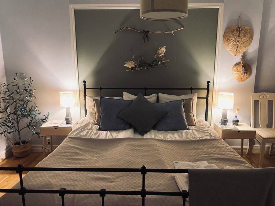 Quarto bem organizado com cama, duas mesas de cabeceira, um criado-mudo, uma planta em vaso e detalhes decorativos nas paredes.