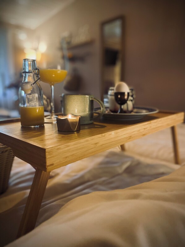 A wooden table with a bottle of orange juice, a candle, and a mug on a bed.