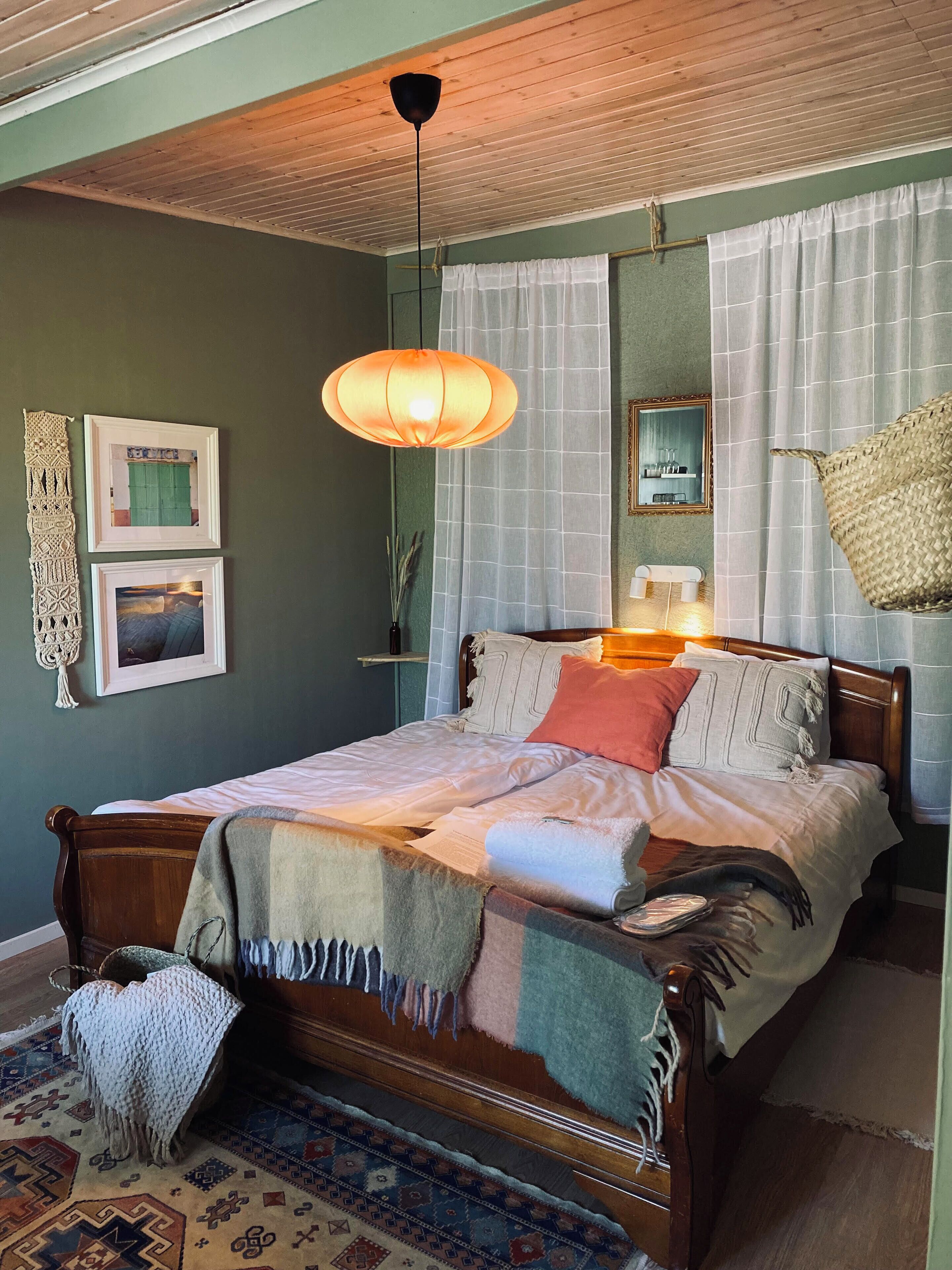 Un dormitorio con una cama de madera, una lámpara colgante, un tapete estampado y cuadros en la pared.