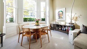 Un comedor con una mesa redonda y sillas, una estantería y un cuadro en la pared.