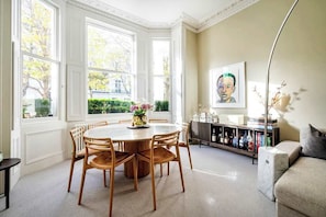 A dining area with a round table and chairs, a bookshelf, and a painting on the wall.