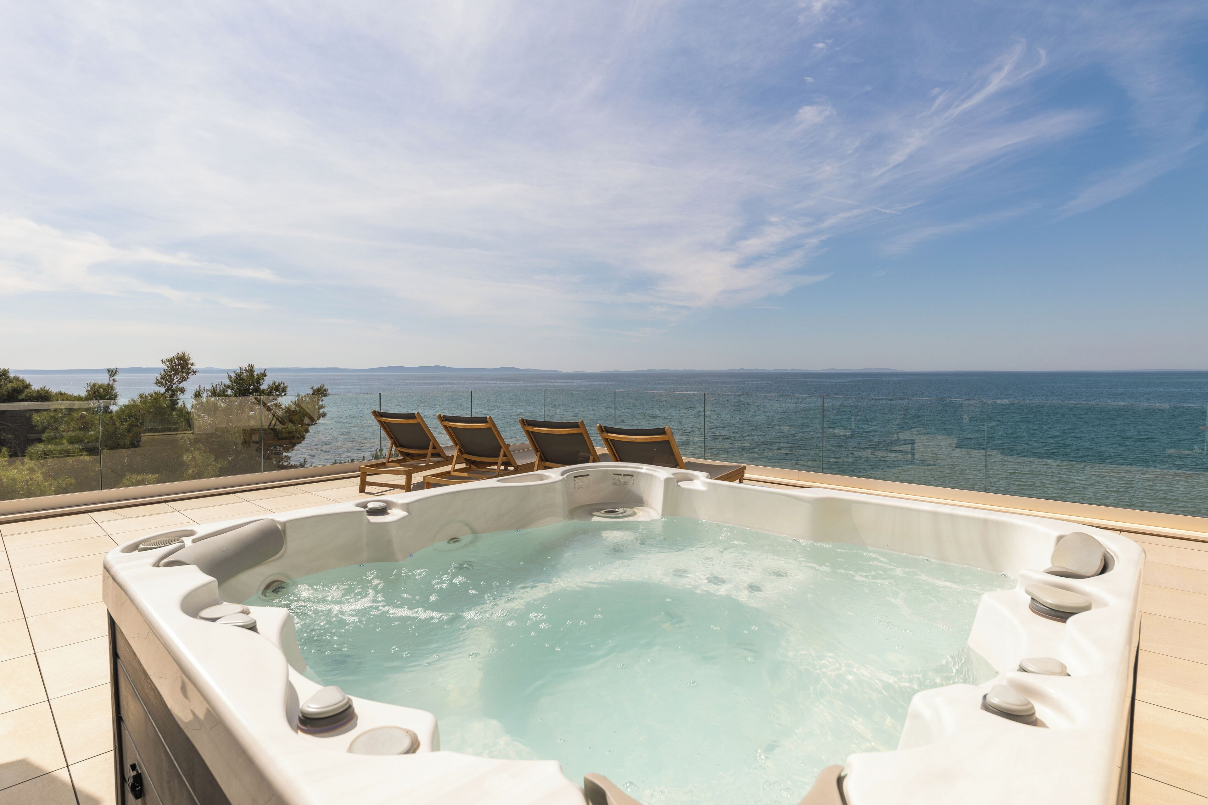 A hot tub with a panoramic sea view, surrounded by lounge chairs.