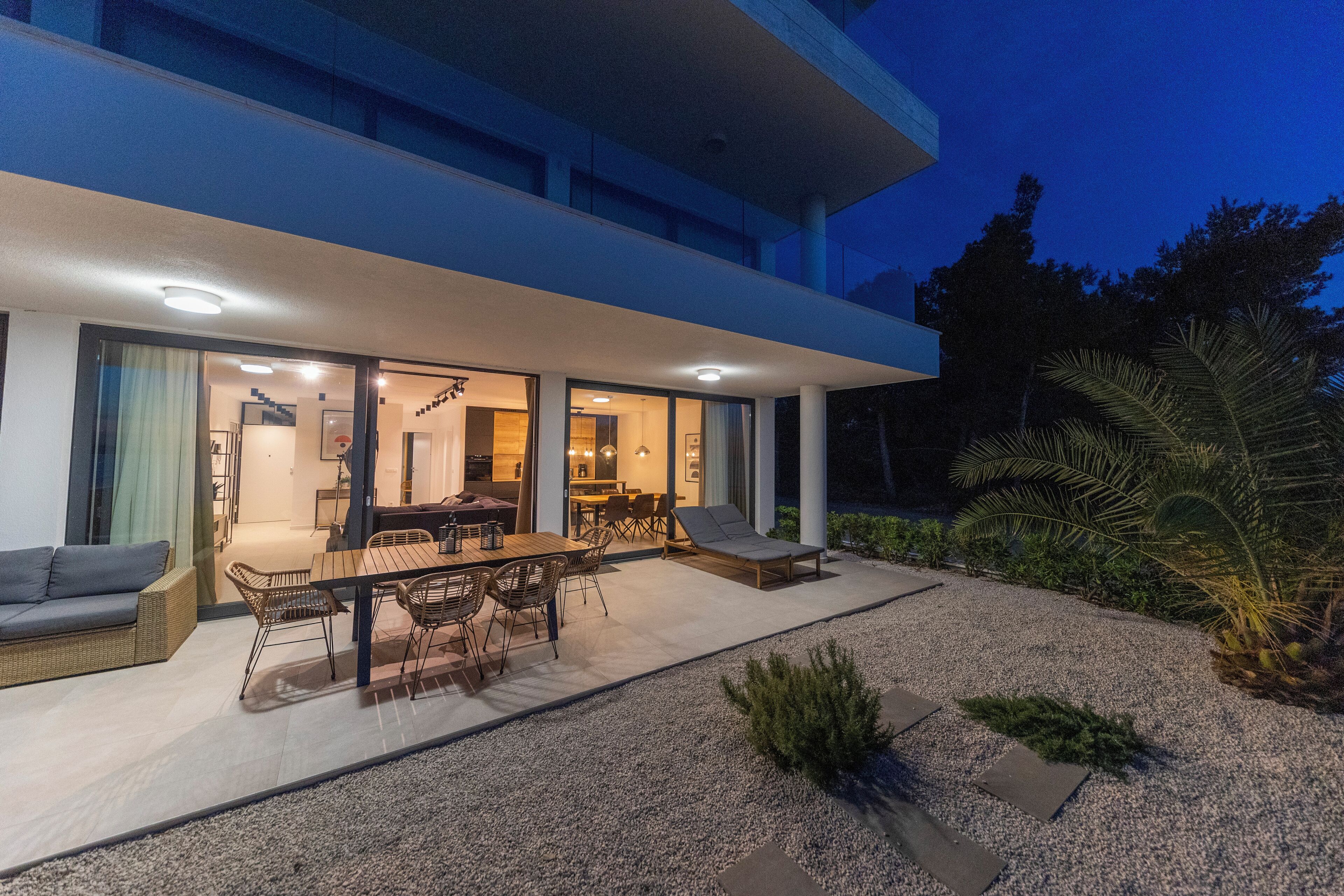 Une maison moderne dotée d’un patio, de mobilier d’extérieur et d’un intérieur bien éclairé.