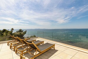 Eine Terrasse mit Holzliegen und einer Glasreling mit Blick auf ein Gewässer.
