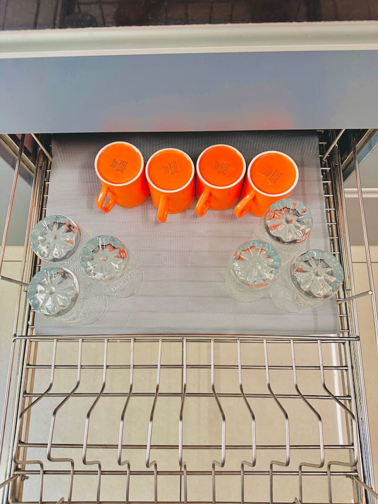 Une cuisine avec un étagère en métal où sont posées des tasses orange et des verres transparents.