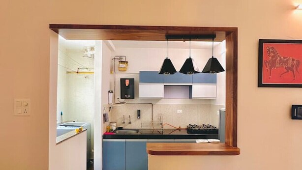 A modern kitchen with blue cabinets, a wooden countertop, and black pendant lights. - Flamingo: 2BHK AC Flat, Near Phoenix Mall Wakad (Pimpri-Chinchwad)