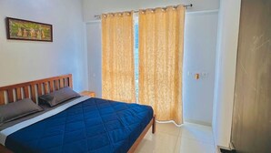 A bedroom with a bed, a ceiling fan, a window with curtains, and a door. - Flamingo: 2BHK AC Flat, Near Phoenix Mall Wakad (Pimpri-Chinchwad)