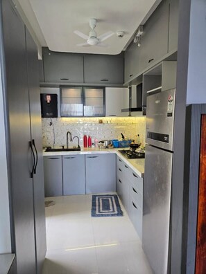 A compact kitchen with grey cabinets, a white ceiling fan, a built-in microwave, and a small window with blinds.
