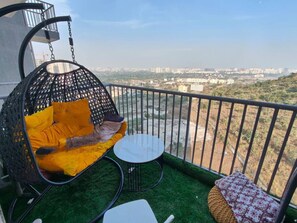 Un balcón con una hamaca colgante, una mesita y vistas a un paisaje urbano.
