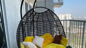 Una silla colgante con cojines amarillos en un balcón con vista a edificios.