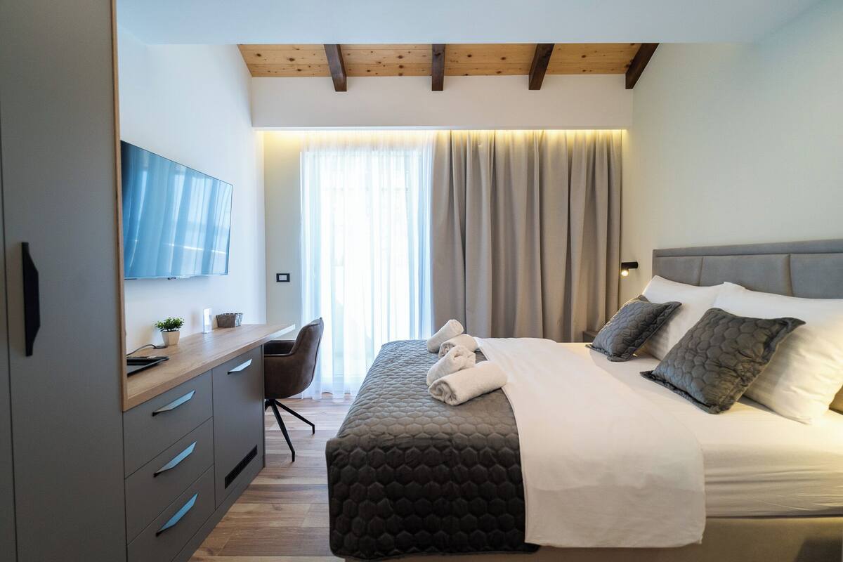 A modern hotel room with a bed, a desk, a chair, and a TV.