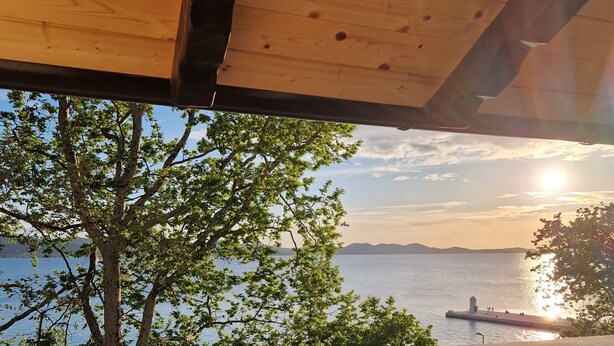 Eine Terrasse mit Tisch für zwei Personen, Blick auf ein Gewässer und ein entferntes Land, mit Holzboden und blauem Himmel.