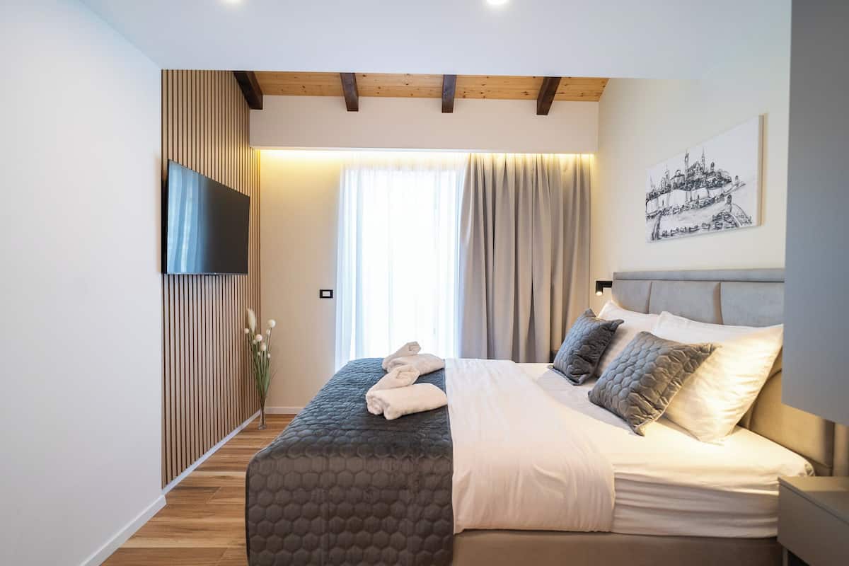 A modern bedroom with a bed, a TV mounted on the wall, and a window with curtains.