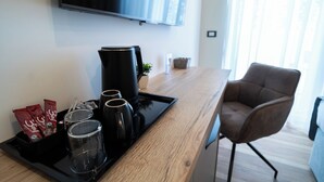Ein modernes Hotelzimmer mit Schreibtisch aus Holz, einer Kaffeemaschine und einem Tablett mit Kaffeetassen und Snacks.