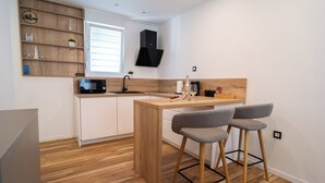 Eine moderne Küche mit einer Holz Arbeitsplatte, einer schwarzen Mikrowelle und einem Einbauofen. Zwei graue Barhocker und ein Holztisch sind ebenfalls vorhanden.