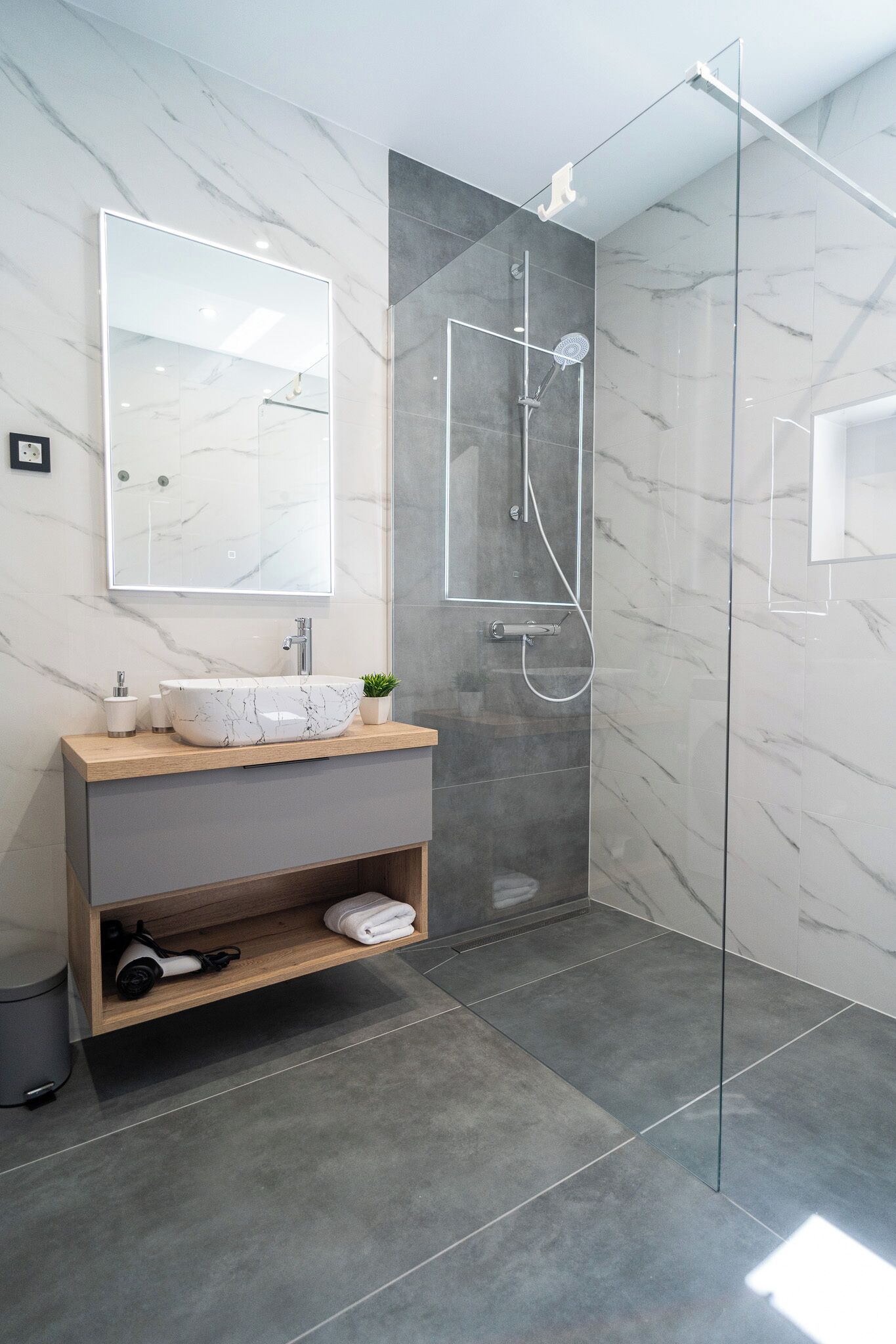 A modern bathroom with a marble vanity, a glass-enclosed shower, and a large mirror.