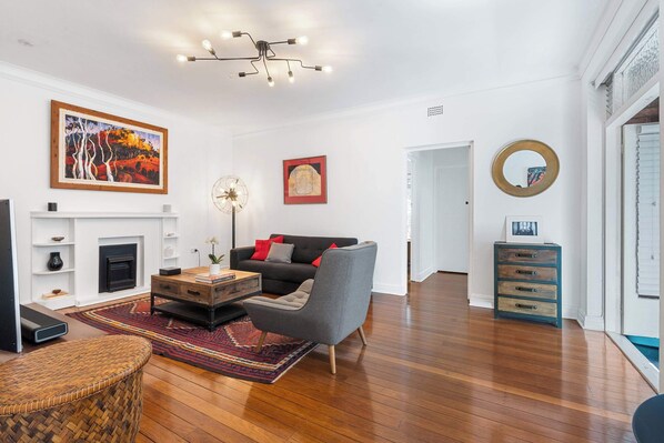 A modern living room with a fireplace, a grey armchair, a coffee table, and a large painting on the wall.