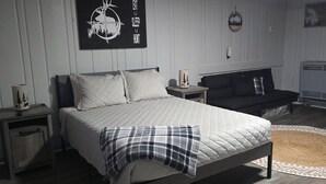 A bedroom with a bed, a nightstand, a dresser, a wall-mounted TV, and a ceiling light.
