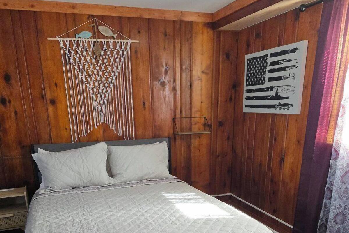 A wooden-paneled bedroom with a bed, a macrame wall hanging, and a framed American flag.