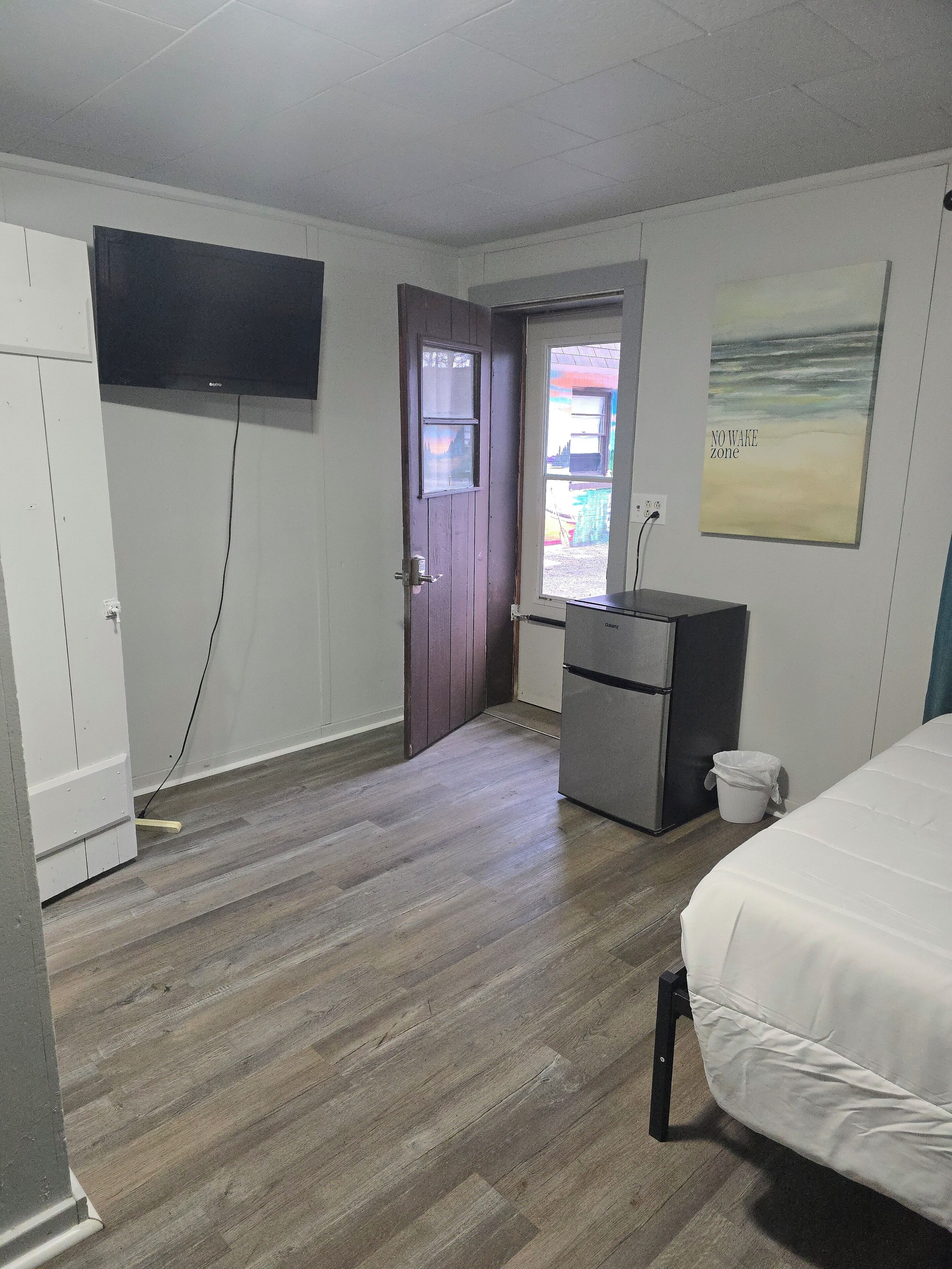 Une chambre d’hôtel équipée d’un lit, d’un bureau, d’une télévision et d’une porte donnant sur un espace extérieur.