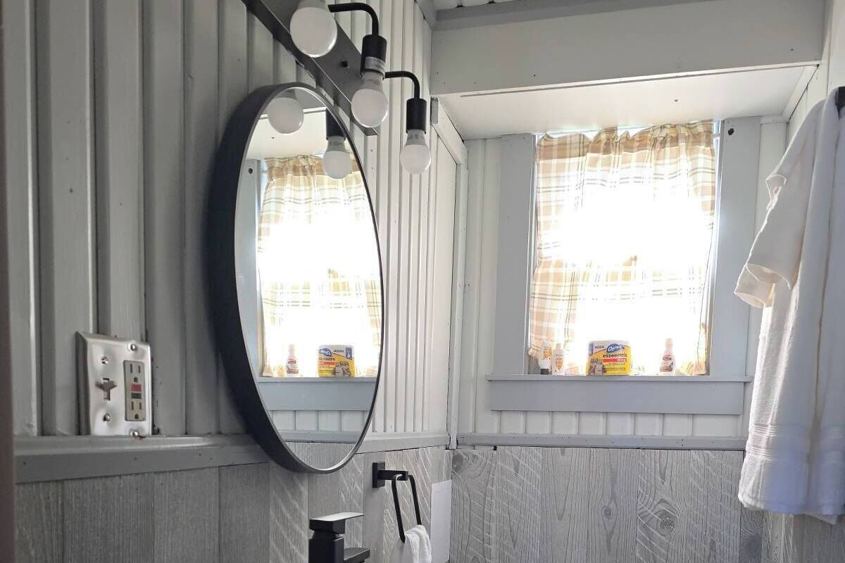 A bathroom with a wooden vanity, a toilet, a sink, a mirror, and a window with curtains.