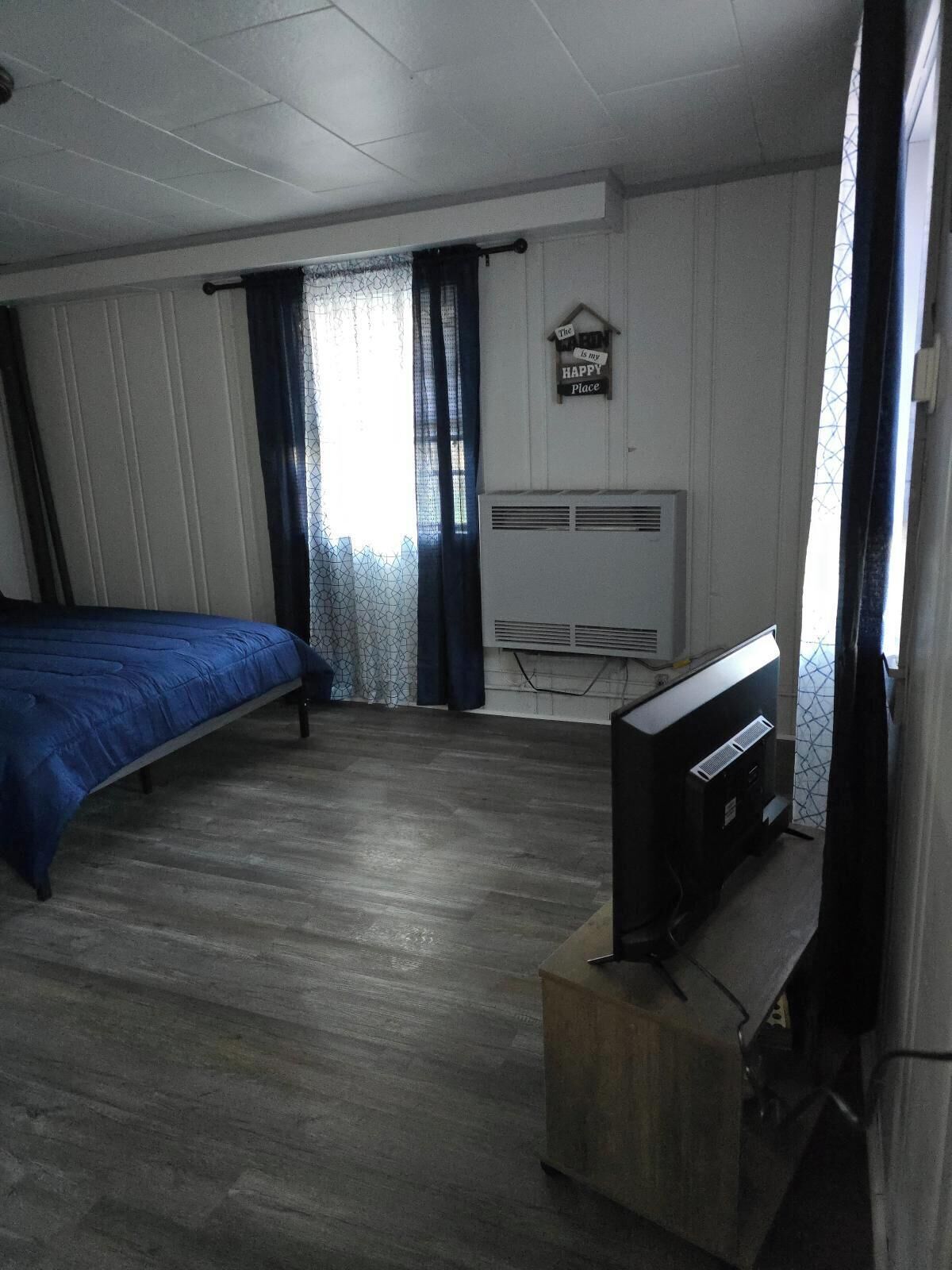 Een kamer met een bed, een televisie op een houten dressoir, een raam met gordijnen en een airconditioner aan de muur.