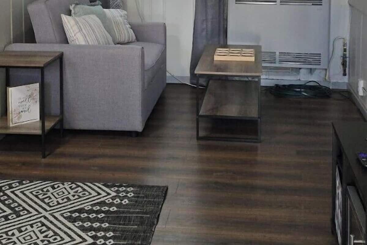 A modern living room with a grey sofa, a coffee table, and a wall-mounted air conditioning unit. A motivational quote and a paddle are visible on the wall.