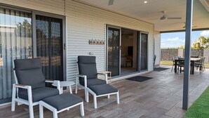 Un patio techado con dos sillones, una mesa y una puerta corrediza de vidrio que da a un espacio interior.