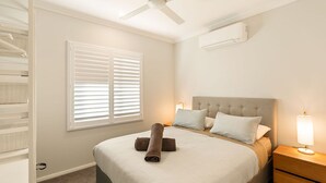 Un dormitorio con cama, mesitas de noche, ventilador de techo y ventana con persianas.