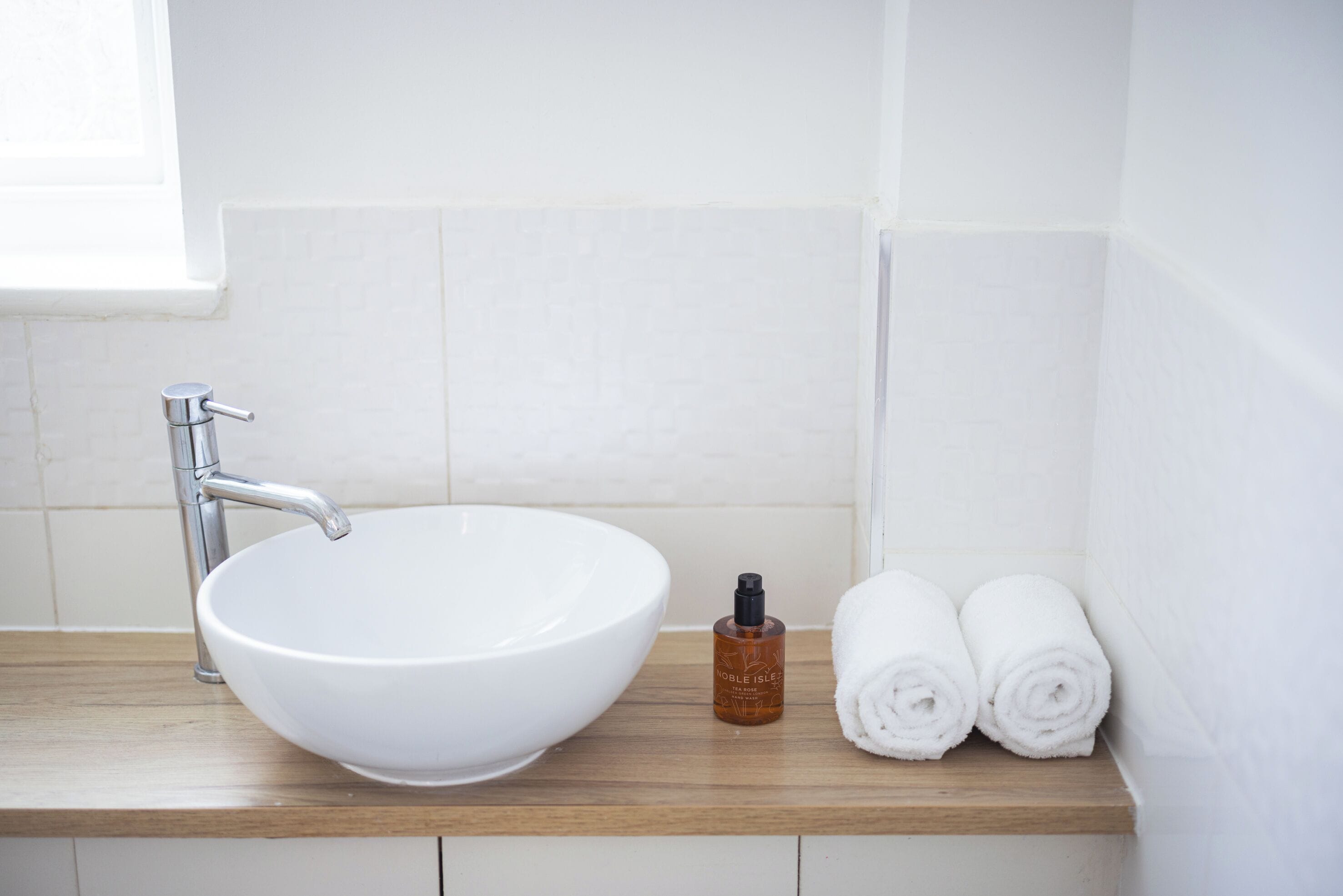 A bathroom with a white sink, a wooden countertop, and two rolled towels.