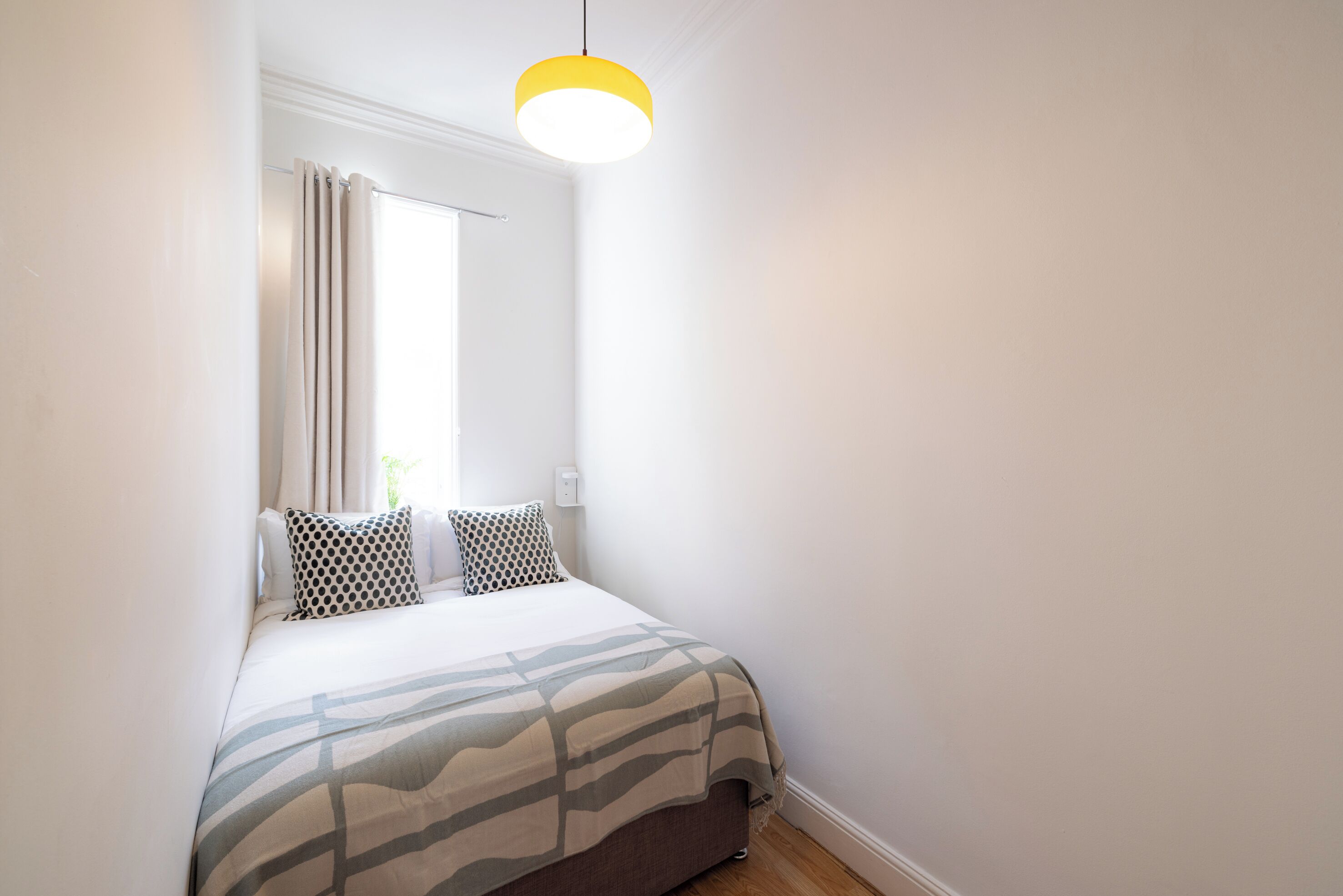 Un dormitorio con cama, ventana con cortinas, lámpara colgante y mesita de noche.