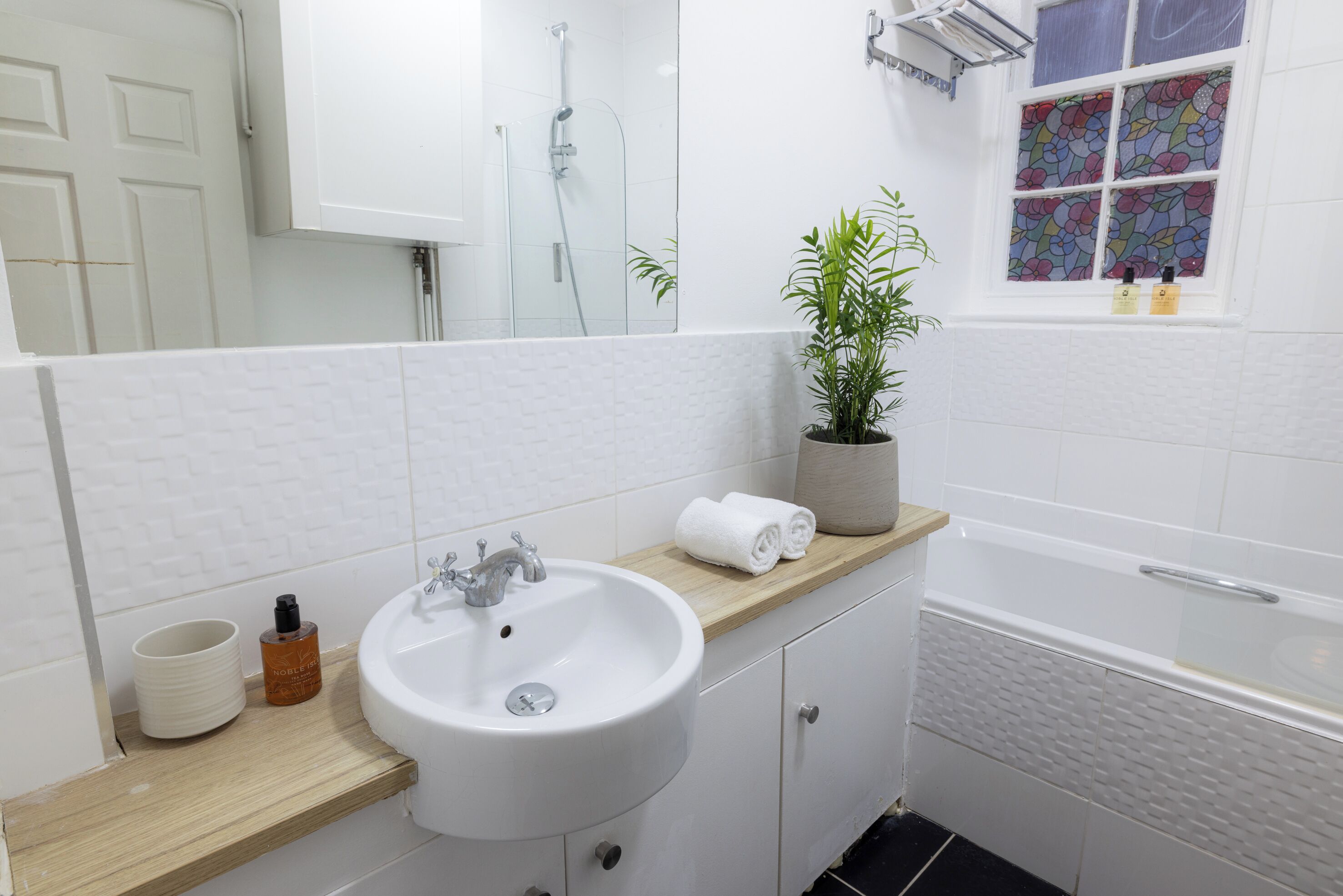 A bathroom with a white sink, wooden countertop, and a potted plant.