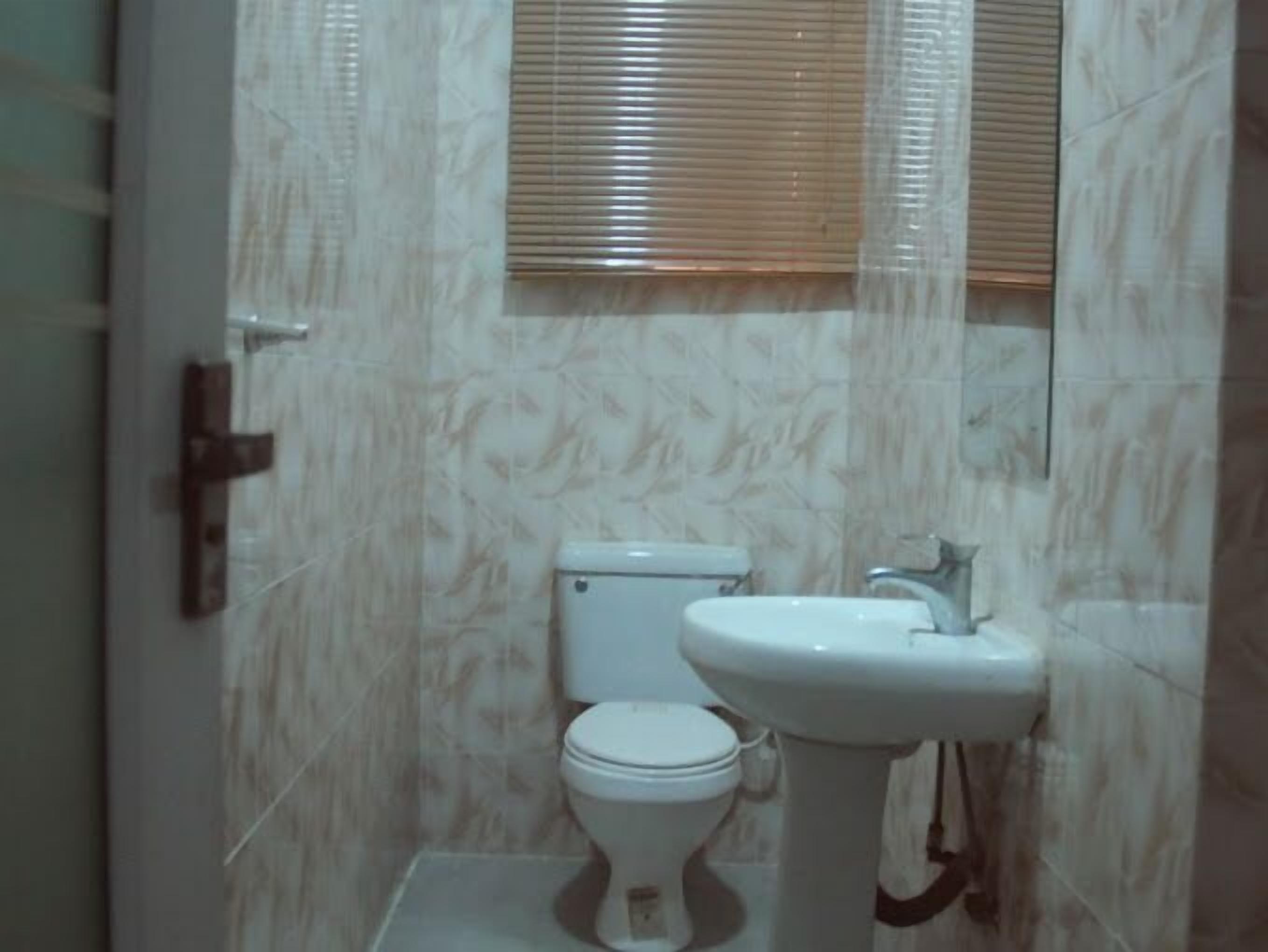 Une salle de bain avec des toilettes, un lavabo et des stores aux fenêtres.