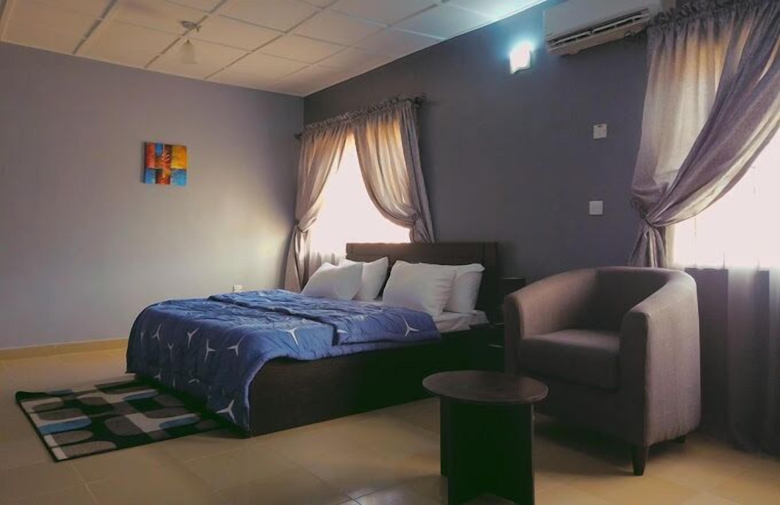 A bedroom with a bed, a chair, a small table, and a painting on the wall.