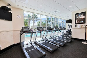 Eine Reihe von Laufbändern in einem Fitnessstudio mit großen Fenstern und Blick auf einen Poolbereich.
