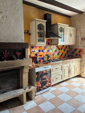 A kitchen with a stone fireplace, colorful tiles, and wooden cabinets.